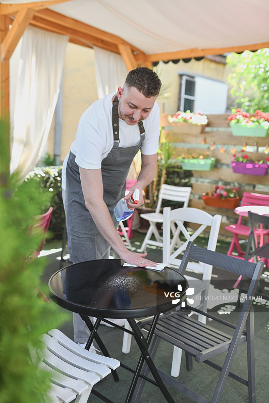 快乐的男性在阳光明媚的咖啡店整理户外座位区图片素材