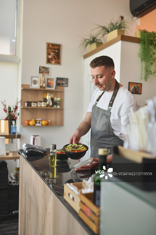 男性食品吧员工在吧台后准备外卖沙拉碗图片素材