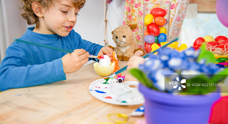 孩子在工艺桌上绘制复活节彩蛋，周围有春季装饰图片素材