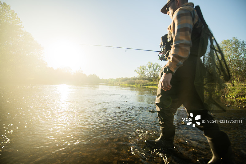 渔夫在金色时光中走在河里，准备去钓鱼。图片素材