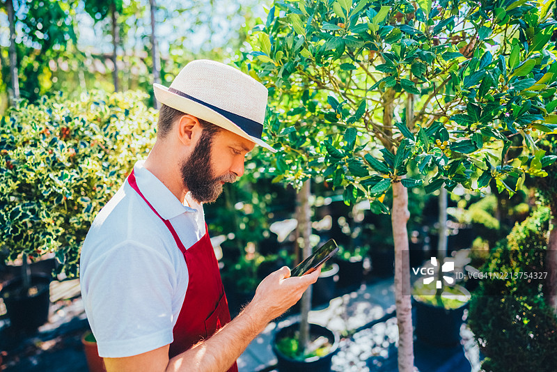 男园丁在户外植物苗圃中使用智能手机图片素材