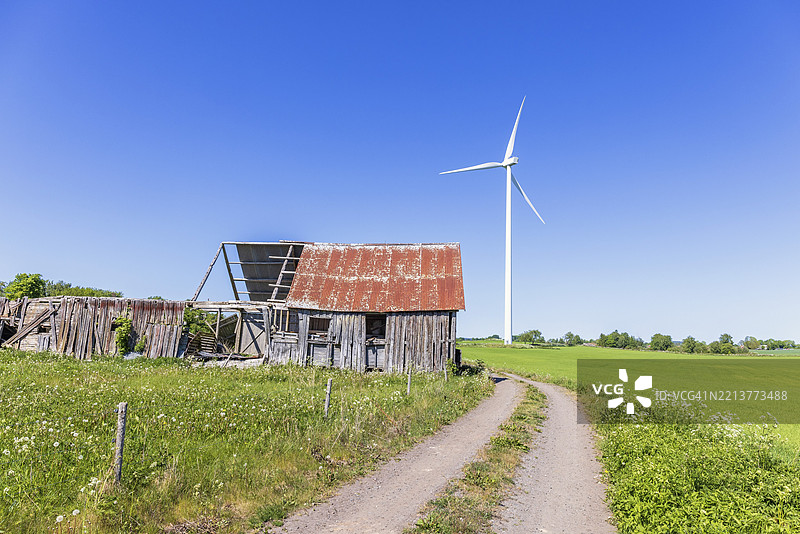 瑞典乡村阳光明媚的夏日，农村风景中一条泥土路旁有一座破旧的谷仓和一座风力发电机。图片素材