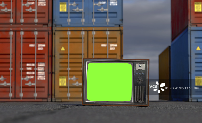 复古电视机与色度绿屏静静地放在装货码头的沥青上，周围是堆叠的集装箱。图片素材