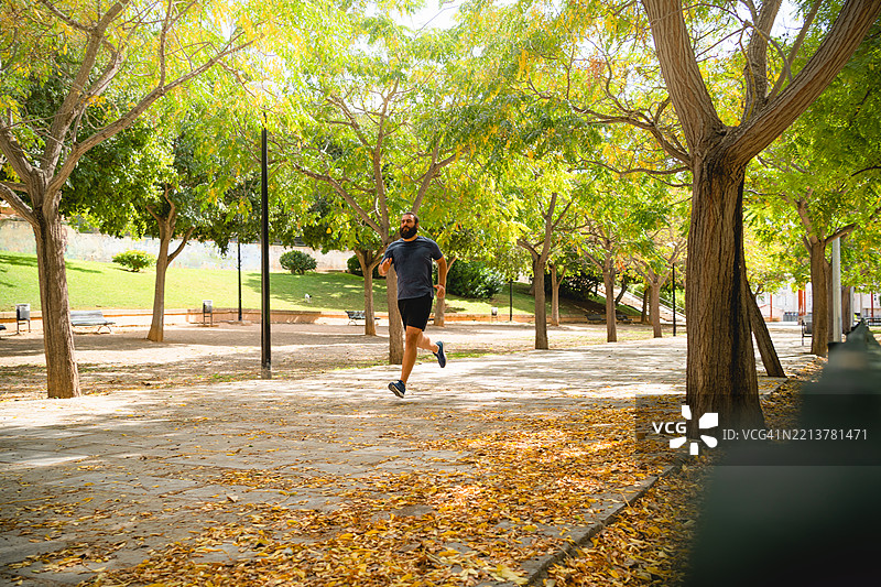 男子在覆盖着落叶的公园小径上慢跑图片素材
