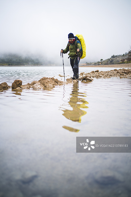 背着背包，手持登山杖的徒步旅行者走过水面图片素材