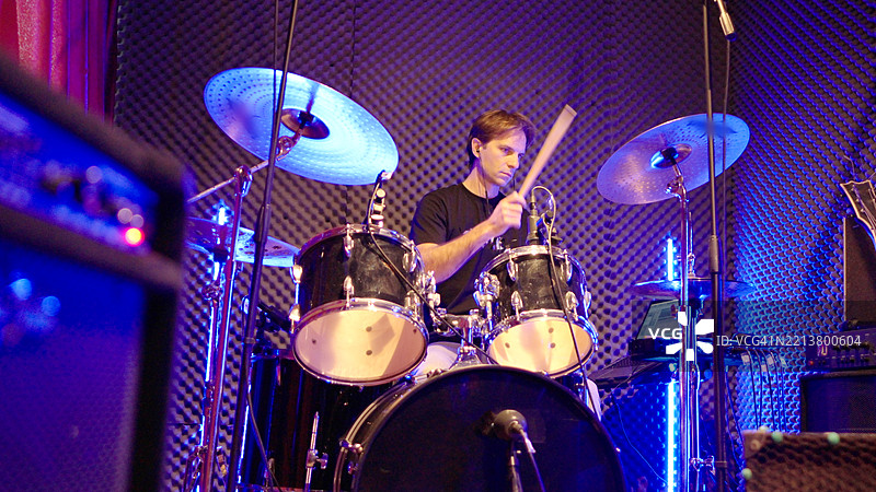 兴奋的鼓手在霓虹灯照明的音乐工作室中独奏图片素材