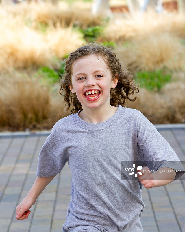 微笑的女孩半身像，前牙歪斜，朝镜头奔跑，背景为户外场景。图片素材