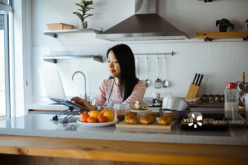 漂亮的亚洲女性在厨房桌子上使用笔记本电脑。图片素材