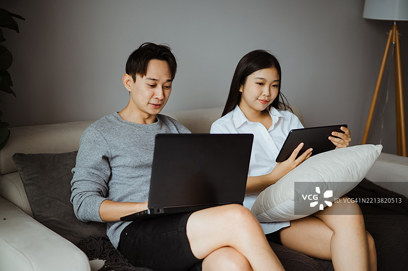 亚洲夫妇在舒适的客厅中使用笔记本电脑和平板电脑图片素材