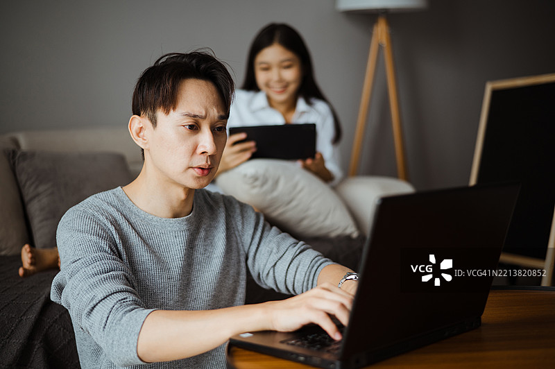 亚洲丈夫在酒店工作，妻子在后面看电视剧。图片素材