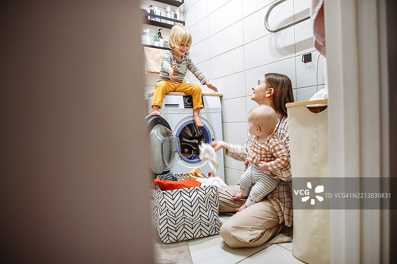 真诚的育儿时刻：母亲在孩子们的洗衣乱象中微笑图片素材