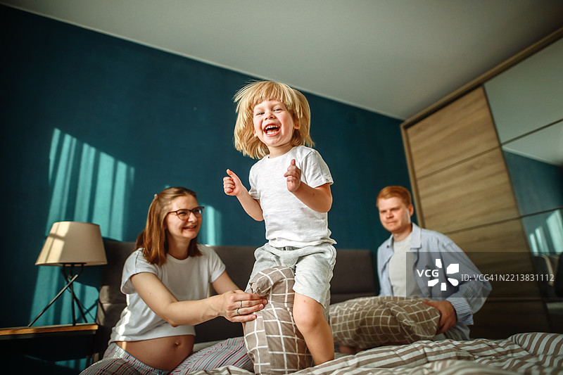 活泼的能量和家庭和谐，金发孩子在床上跳跃，父母共享快乐时光。图片素材
