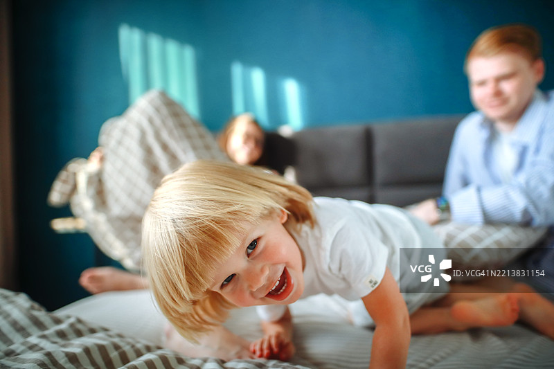 金发幼儿与父母在床上，展现了快乐童年和家庭纽带的真实喜悦。图片素材