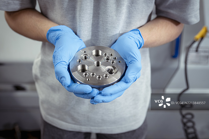 工程师在小型工程厂房中手持复杂的金属零件图片素材