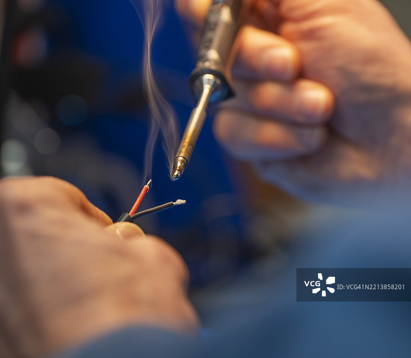 熟练的技术员在工作坊中焊接电线，傍晚时分，焊接铁冒出烟雾。图片素材