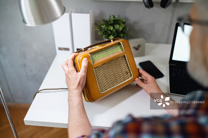 中年男子在现代工作空间中检查一台复古收音机图片素材