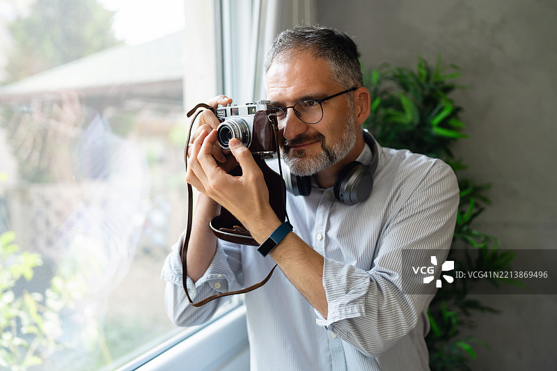 中年男子在大窗户旁使用复古胶卷相机。图片素材