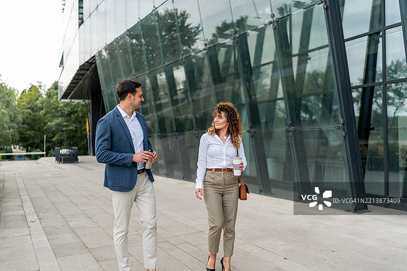 商业伙伴在现代玻璃办公楼前走动并交谈图片素材