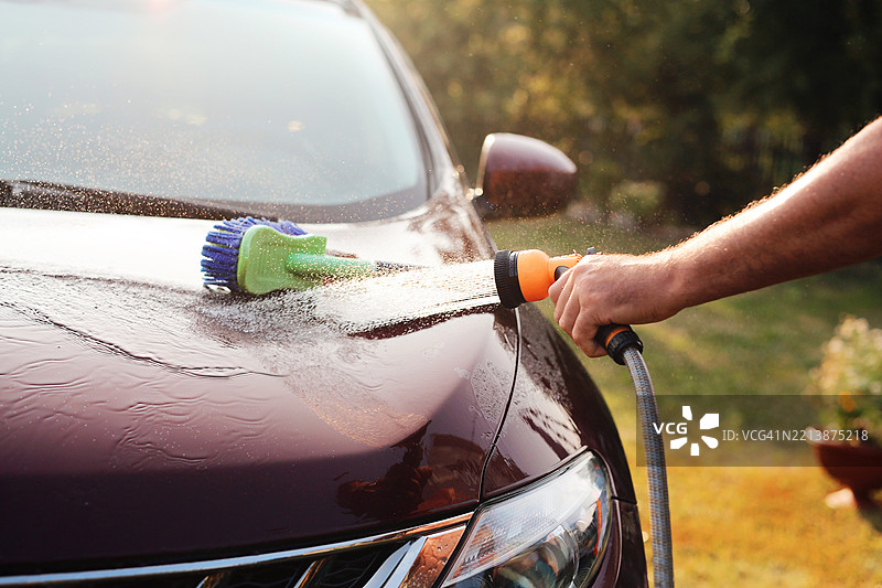 一名男性司机在大自然中用水管洗车图片素材