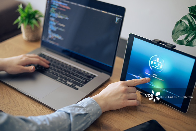 女商人与平板电脑上的人工智能助手互动，同时进行笔记本电脑工作。图片素材