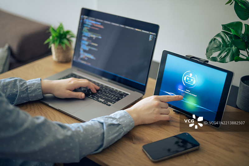 女商人与平板电脑上的人工智能助手互动，同时进行笔记本电脑工作。图片素材