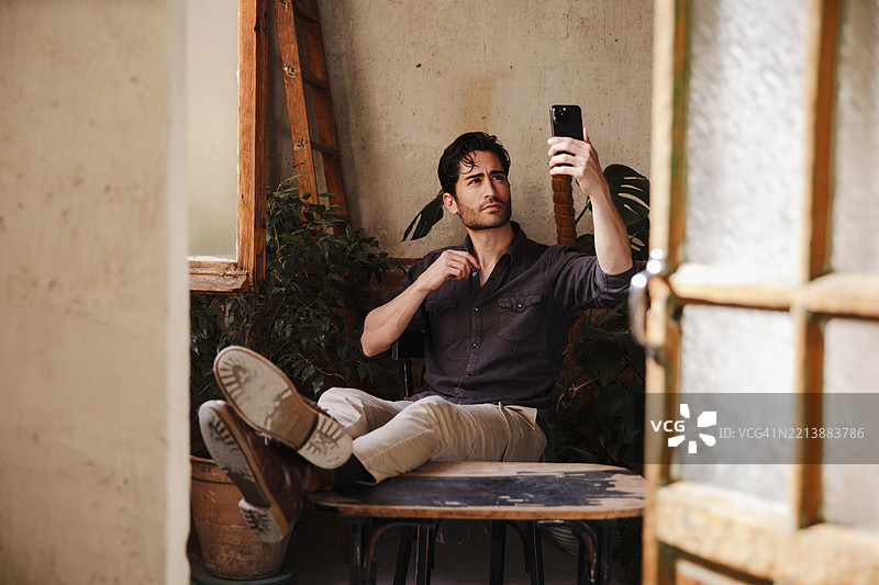 一位留着三天胡须的帅气男士坐着用手机自拍图片素材