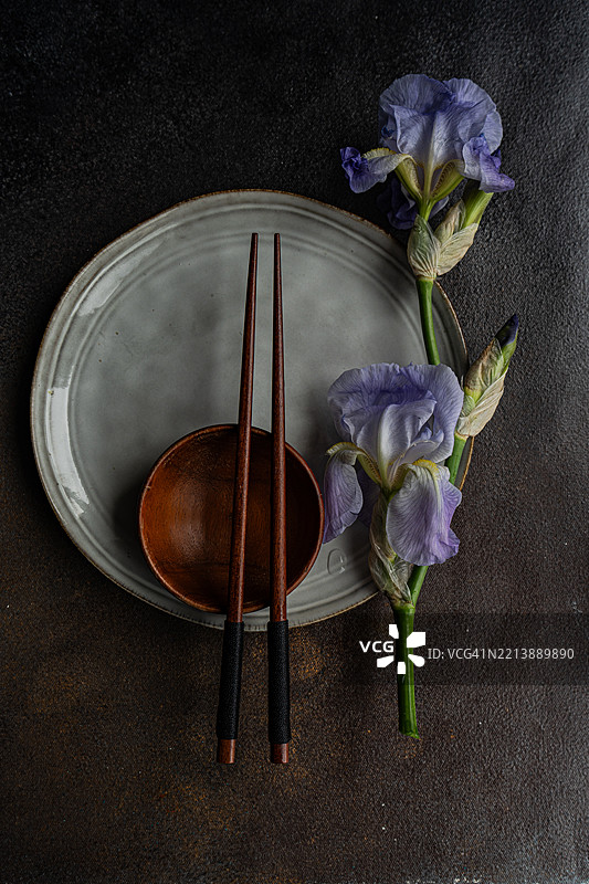 俯视角度的特写镜头，展示了一个亚洲餐具摆设，配有筷子和淡蓝色的鸢尾花。图片素材