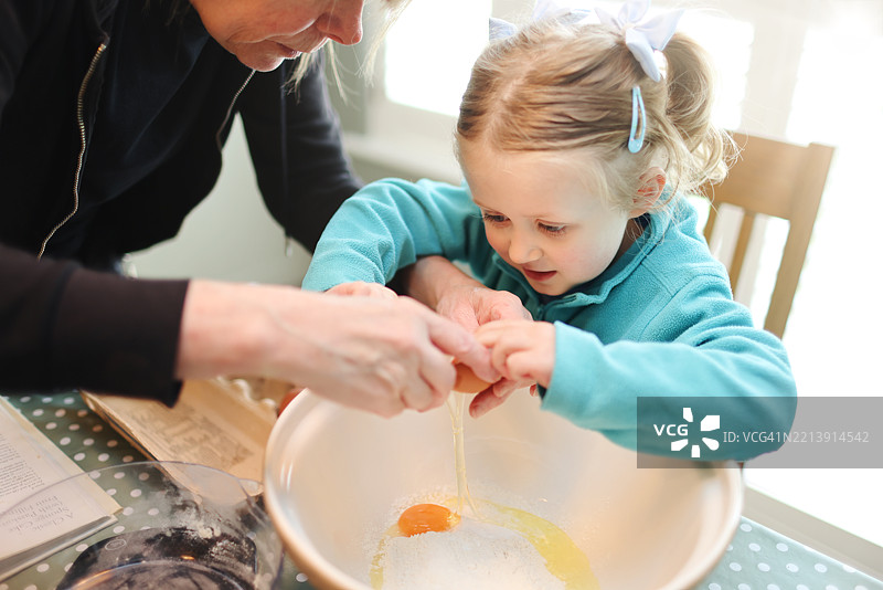 四岁的小女孩在奶奶的帮助下学习如何打蛋，一起烤蛋糕。图片素材