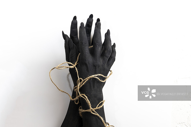 概念照片：女人的手涂有黑色油漆，手上缠绕着绳子。图片素材