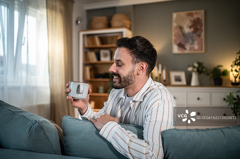 年轻男子在舒适的客厅里放松，享受一杯咖啡或茶图片素材