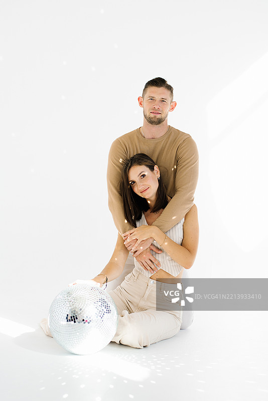 年轻的男女在背景中有一个迪斯科球的情况下摆姿势拍照，场景轻松愉快，情侣们相拥享受这一刻。图片素材