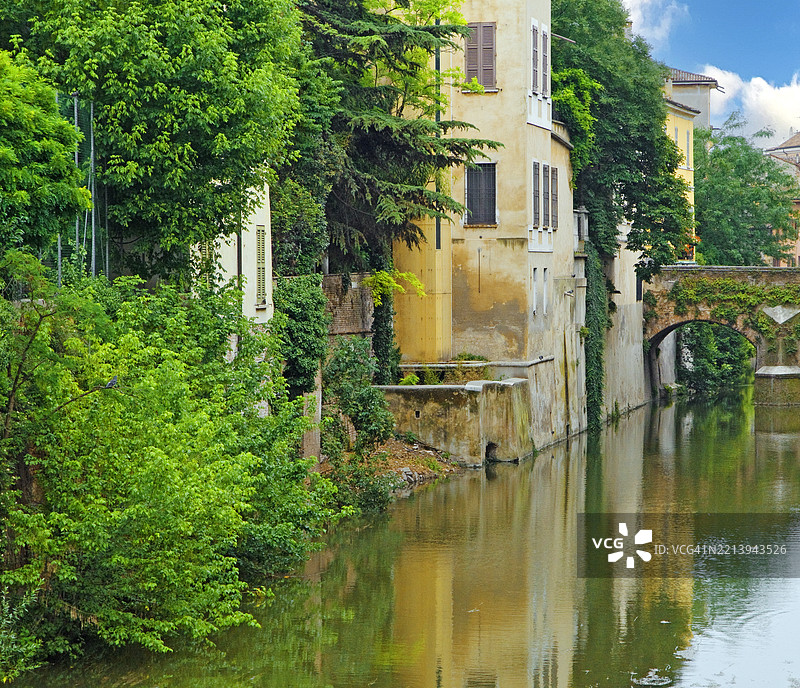 曼托瓦老城中的运河，四周环绕着古老建筑和郁郁葱葱的绿植图片素材