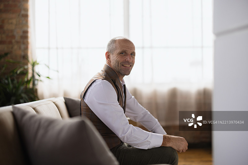 微笑的成熟商人在现代办公室的沙发上放松。图片素材