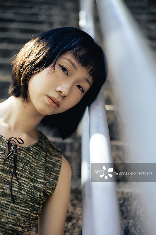 年轻的亚洲女性靠在楼梯扶手上，注视着镜头的特写肖像图片素材