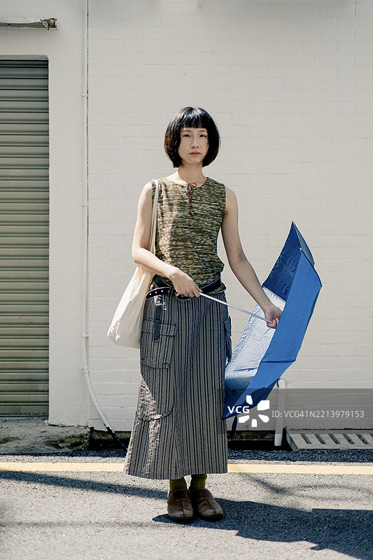 年轻的亚洲女性在白天的城市街道上撑着蓝色雨伞图片素材