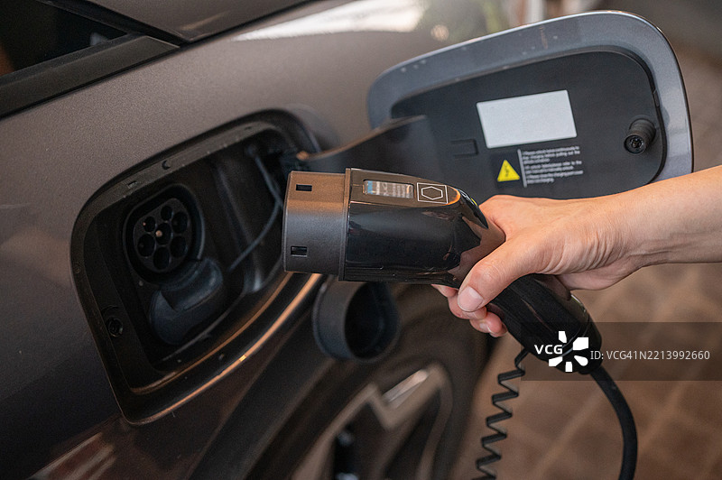 电动车司机插入电连接器为电动车充电的特写镜头。图片素材