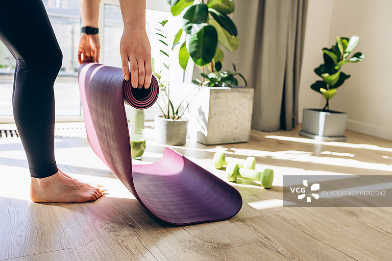 年轻女性在家练习瑜伽，特写镜头。正在展开瑜伽垫，准备开始锻炼。图片素材