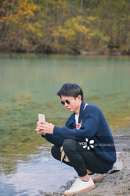 日本亚洲男性在秋季的上高地国家公园享受旅行视频博客，用智能手机捕捉秋天森林的色彩。图片素材