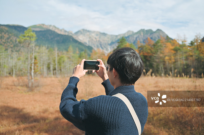 日本亚洲男性在秋季的上高地国家公园享受旅行视频博客，用智能手机捕捉秋天森林的色彩。图片素材