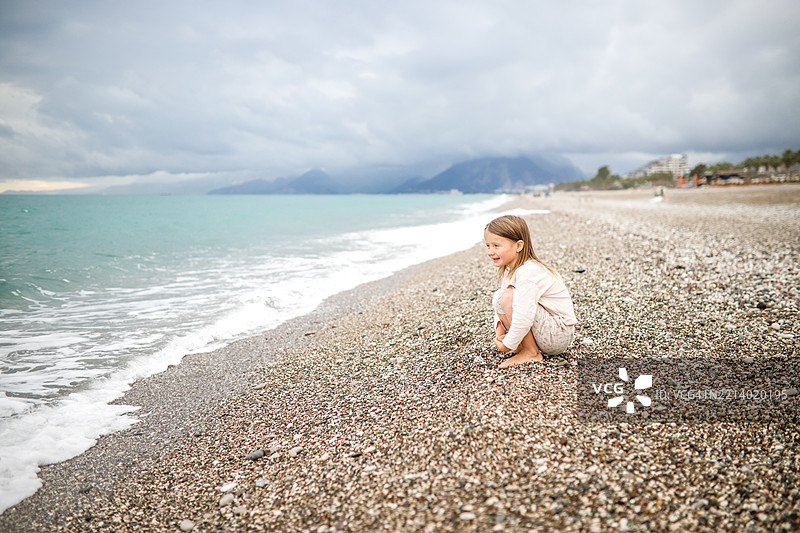 穿着长袖上衣和卷起裤子的女孩在海滩上，享受着真实的童年时光。图片素材