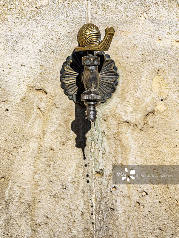 街道上的旧公共饮水喷泉，水龙头开着，水滴滴落。图片素材