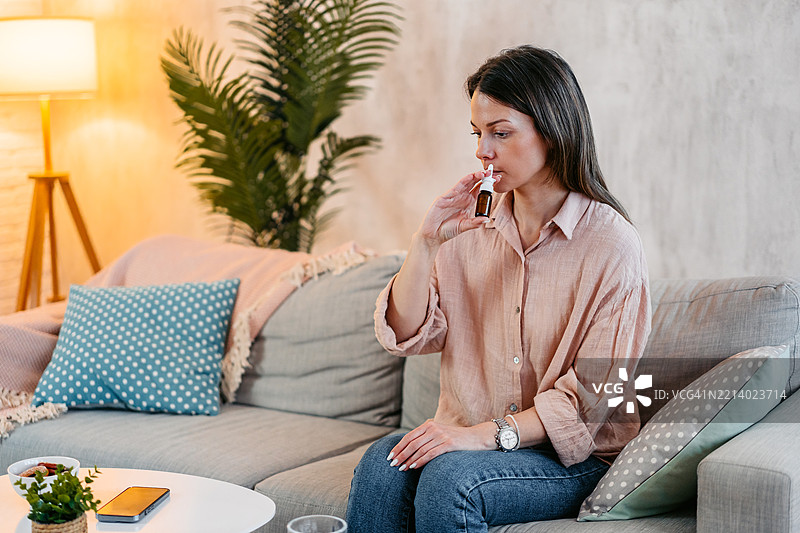 年轻女性在家沙发上使用鼻喷剂图片素材