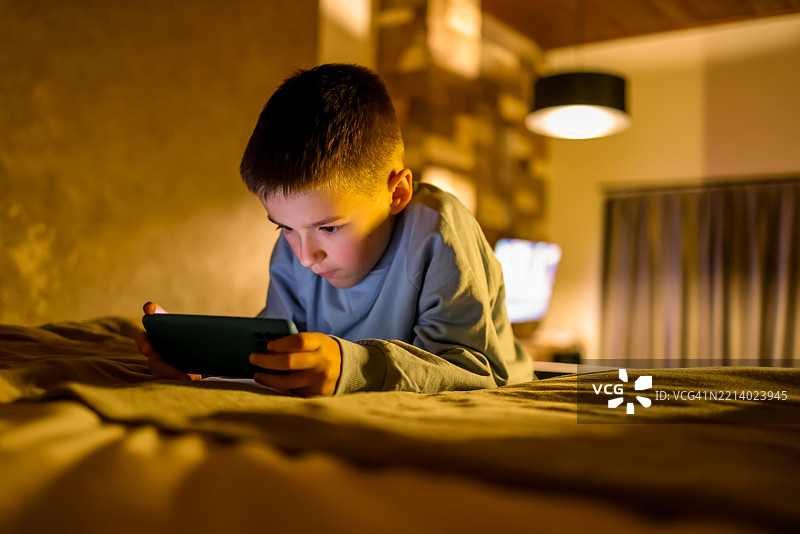 年轻男孩在现代卧室里躺着玩智能手机图片素材