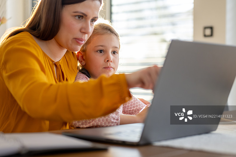 年轻的白人母亲在家工作，同时与她好奇的女儿互动图片素材