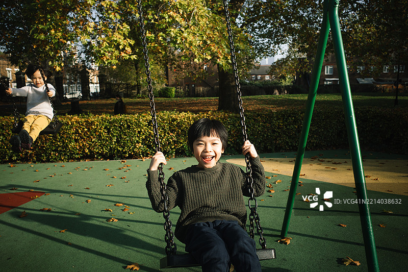 可爱的小男孩在游乐场的秋千上快乐地玩耍，朝着镜头微笑。图片素材