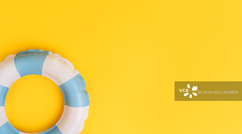 在明亮的黄色夏季背景下，角落里有一个白色和蓝色条纹的游泳圈图片素材