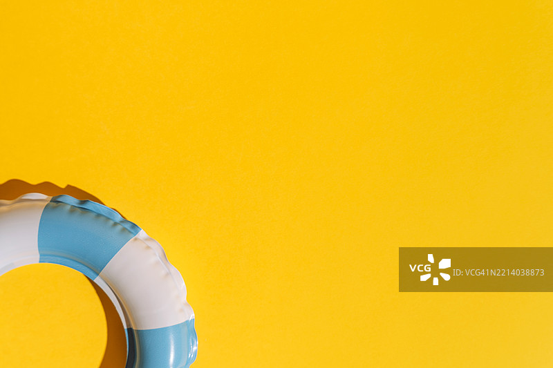 在明亮的黄色夏季背景下，角落里有一个白色和蓝色条纹的游泳圈图片素材