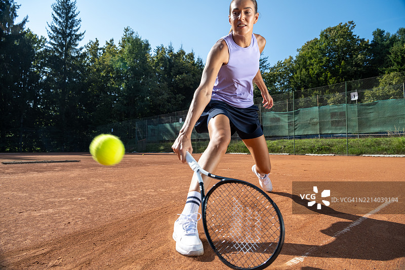 年轻的白人女性网球运动员在阳光明媚的户外红土场上练习图片素材