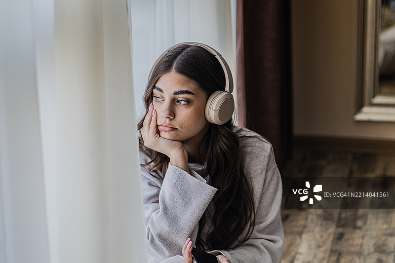 一位神经多样性的美丽年轻女性，患有注意力缺陷多动障碍，戴着耳机坐在窗边休息，聆听轻松的音乐。宁静的时刻在安静的地方。图片素材