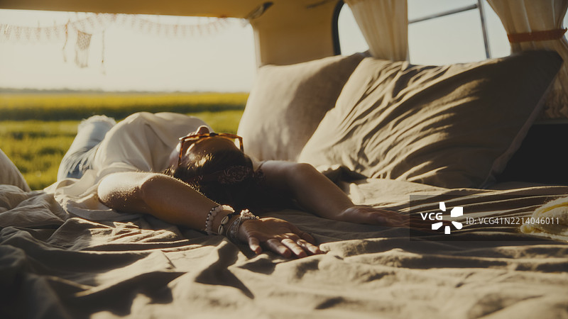 年轻女性在露营车床上放松，享受日落。图片素材